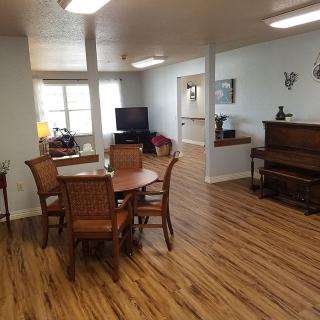 A cozy living and dining area featuring wooden flooring, a piano, and a television.