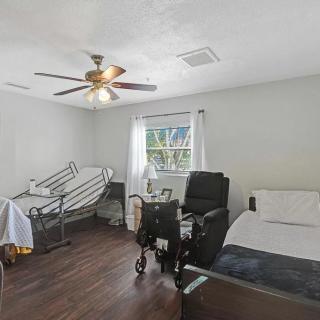 A room with a hospital bed, wheelchair, and a ceiling fan near a window.