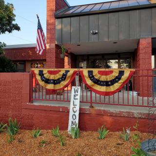 A building entrance decorated with patriotic bunting and a welcome sign, alongside an American flag.