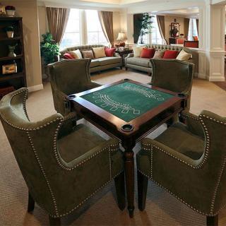 A stylish living room featuring a poker table surrounded by green upholstered armchairs and elegant couches with red cushions.