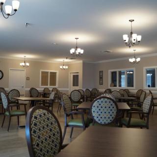 A spacious dining room with several tables and chairs, softly lit by chandeliers.