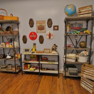 A room with vintage decor featuring shelves filled with books and various collectible items, including a globe and wall art.