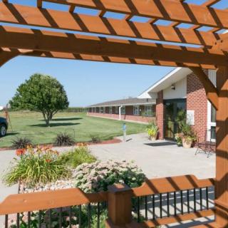 A building with a garden view framed by a pergola, featuring a tree on a sunny day.