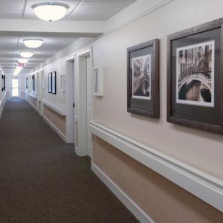 A long, carpeted hallway with framed pictures on the walls and overhead lighting.