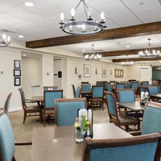 A modern dining area featuring elegant chandeliers and wooden beams, with neatly arranged tables and chairs.
