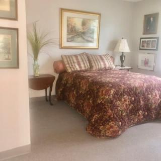 A cozy bedroom with a patterned bedspread, artwork on the walls, and a side table with a lamp.