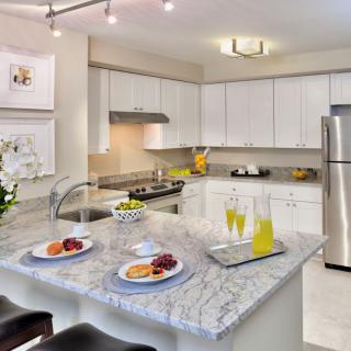 A modern kitchen with white cabinets, stainless steel appliances, and a granite countertop breakfast bar.