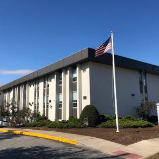 A modern building with an American flag waving in the foreground against a clear blue sky.