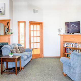 A cozy living room featuring soft blue sofas, a bookshelf filled with books, and a TV mounted above a fireplace.