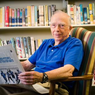 A man sitting in an armchair reading a publication in a library.