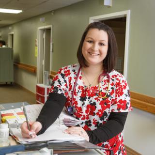 A nurse in colorful scrubs smiling while taking notes in a hospital setting.
