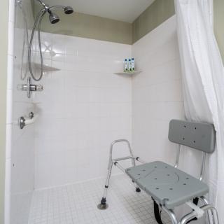 An accessible shower with a safety chair and white curtain.