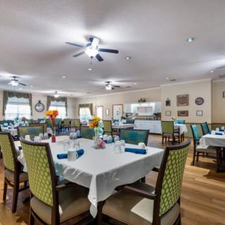 A well-decorated dining area with multiple tables set for a meal, featuring chairs, flowers, and ample lighting.