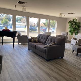 A spacious and well-lit living room featuring a sofa, grand piano, and large windows.