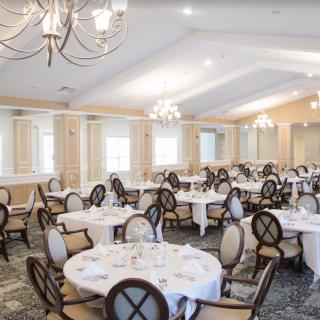 An elegant banquet hall set up with round tables and chairs, featuring chandeliers and a spacious layout.