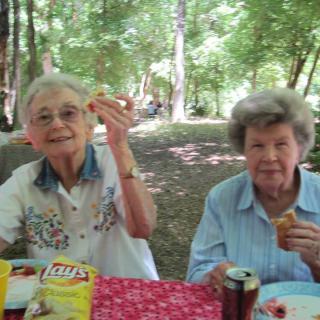 Two elderly women enjoying a picnic in a wooded area.