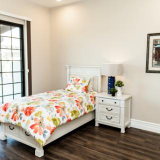 A bright and cheerful bedroom featuring a single bed with colorful floral bedding and white furniture.