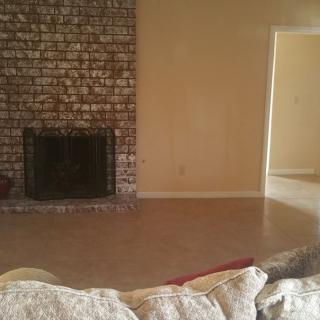 An empty living room with a brick fireplace and neutral walls.