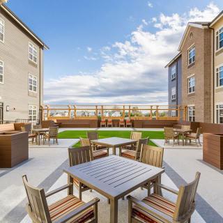 A spacious outdoor patio area surrounded by apartment buildings with tables and chairs, under a partly cloudy sky.