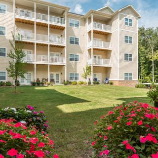 A modern apartment building with balconies, surrounded by a well-maintained garden with vibrant flowers.