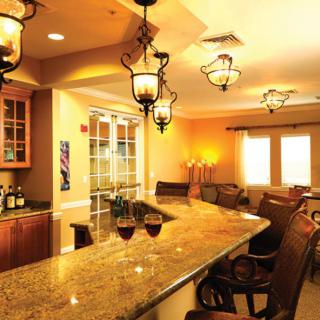 A cozy bar area with a granite counter, warm lighting, and wine glasses on display.