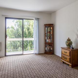 A bright living room with a sliding glass door leading to a balcony, featuring carpeted flooring and wooden furniture.