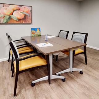 A small conference room with a meeting table, four chairs, and artwork on the wall.