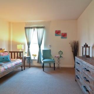 A cozy bedroom with a comfortable armchair, a window with curtains, and a wooden dresser.