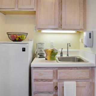 A compact kitchen area with a sink, countertop, and cabinets, featuring kitchen appliances and a fruit bowl.