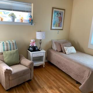 A cozy and inviting bedroom featuring a single bed, comfortable armchair, and decorative artwork.