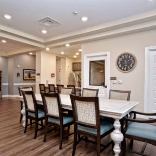 A well-lit dining room with a large table and multiple chairs, featuring elegant decor and wood flooring.