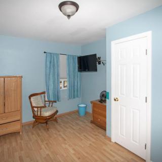 A cozy bedroom with blue walls features a rocking chair, wardrobe, television, and wooden flooring.