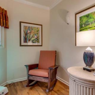 Cozy corner with a wooden chair, lamp on a table, and framed art on the walls.