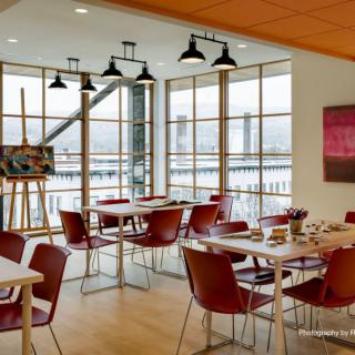 A modern dining area with large windows, featuring tables set for guests and artwork on display.