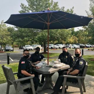 Four police officers seated at a patio table under an umbrella, wearing masks.