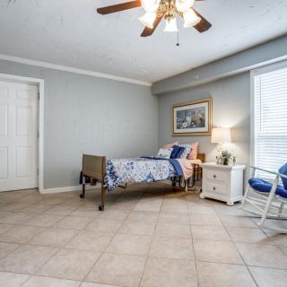 A minimalist bedroom with a single bed, ceiling fan, and tile flooring.