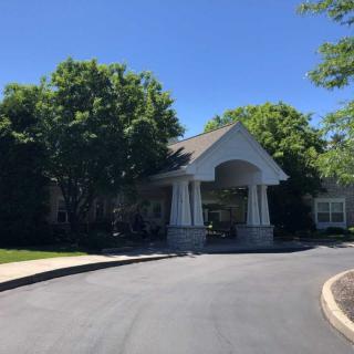 A building with a covered entrance and driveway surrounded by trees on a sunny day.