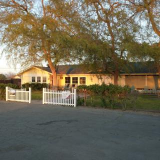 A rural house with a white fence and trees at sunset.