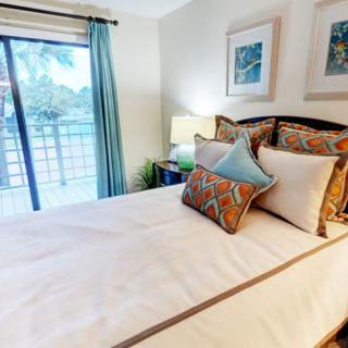 A cozy bedroom with a neatly made bed and colorful pillows, featuring a window with curtains and decorative artwork on the walls.