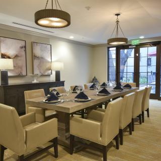 A modern, elegantly designed dining room with a large table and upholstered chairs, featuring contemporary lighting and artwork.