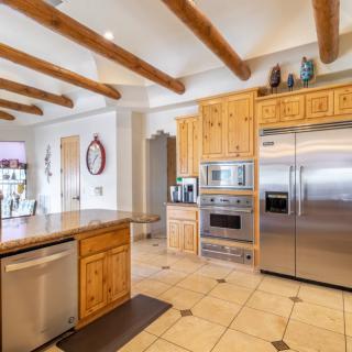A modern kitchen featuring wooden cabinets and stainless steel appliances, with a beamed ceiling and tile flooring.
