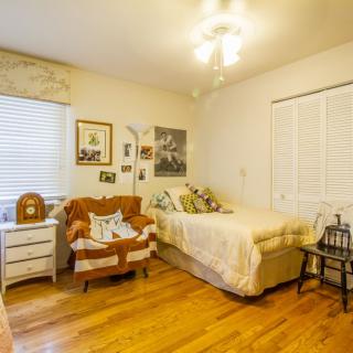 A cozy bedroom with warm lighting, featuring a bed, armchair, and wooden flooring.