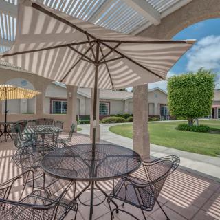Outdoor patio with tables, chairs, and umbrellas under a pergola on a sunny day.