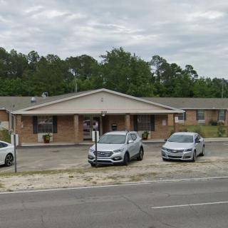 A one-story brick building with a small parking lot and several cars parked in front on a cloudy day.