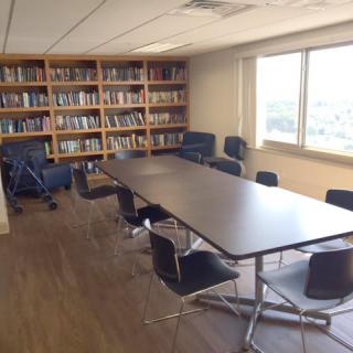 A conference room with a long meeting table surrounded by chairs and bookshelves along the wall.