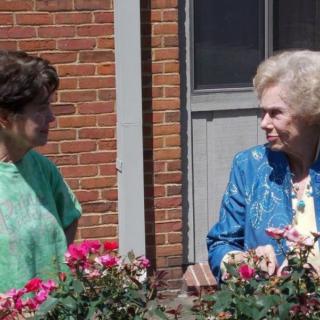 Two women having a conversation on a balcony with flowers.