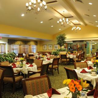 A beautifully decorated restaurant dining room with neatly arranged tables and chairs, adorned with floral centerpieces and elegant lighting.
