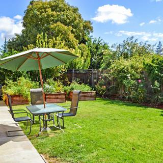 A serene garden with a green lawn, patio furniture, and an umbrella under a clear blue sky.