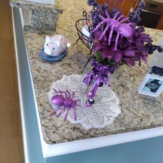 A whimsical purple-themed kitchen centerpiece featuring decorative spiders and flowers.