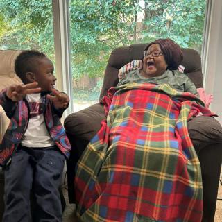A joyful interaction between a child and an elderly person wrapped in a colorful blanket.